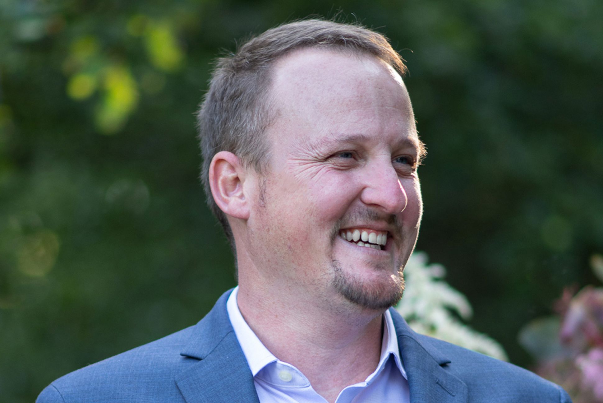 A white male wearing a blue blazer smiling