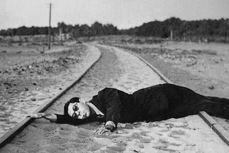 A man in a sunglass and a suit lying on a track covered with sand.