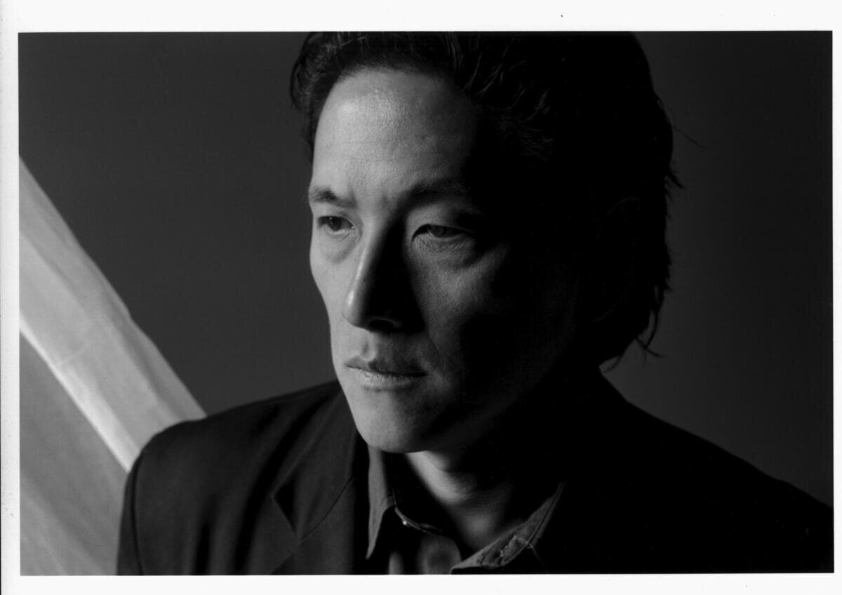 Black and white portrait of Li-Young Lee wearing a suit. Lee is not facing the camera and looks off and to the side.