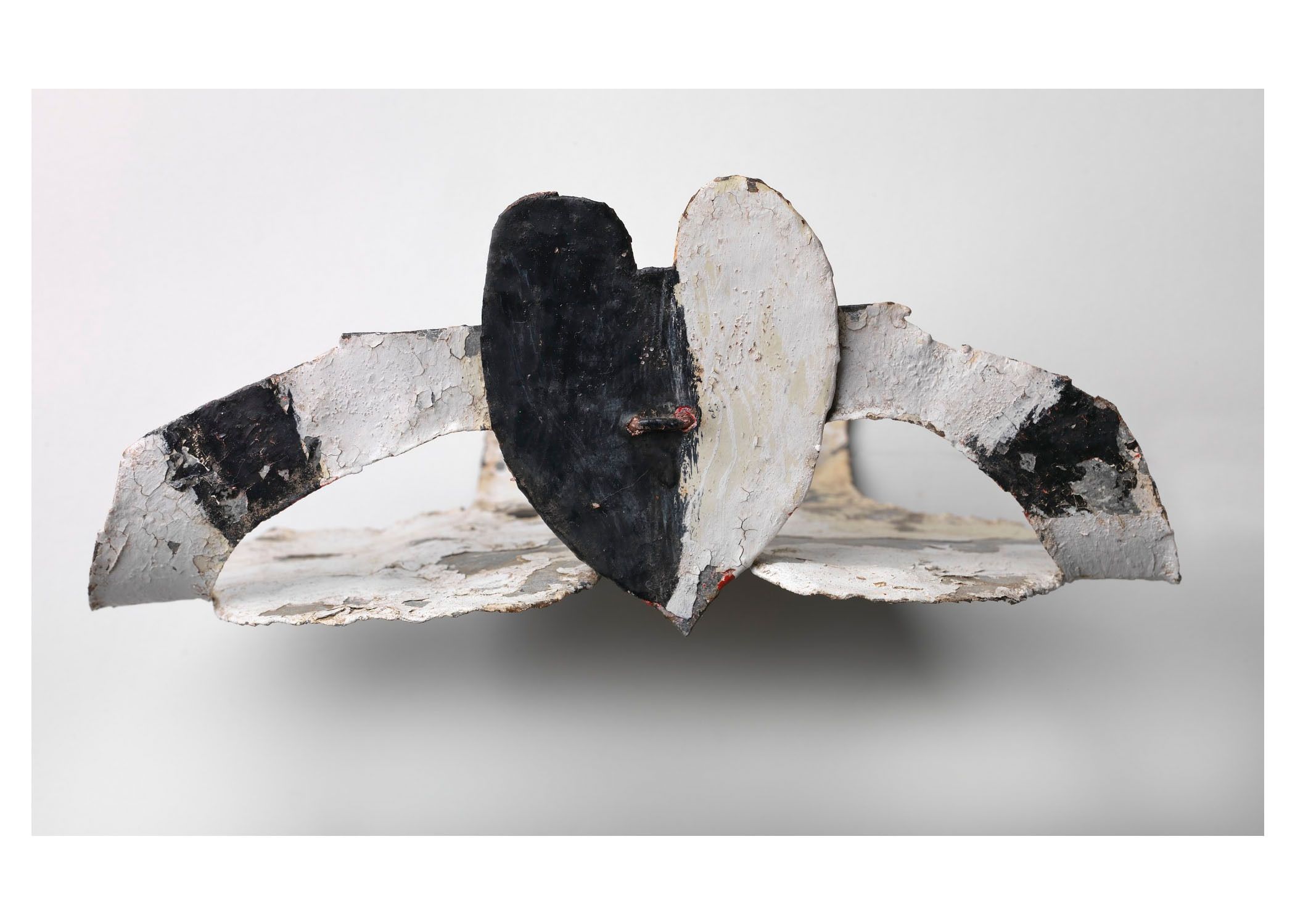 Black-and-white painted heart made of tin, against tin backing, also painted in black and white.