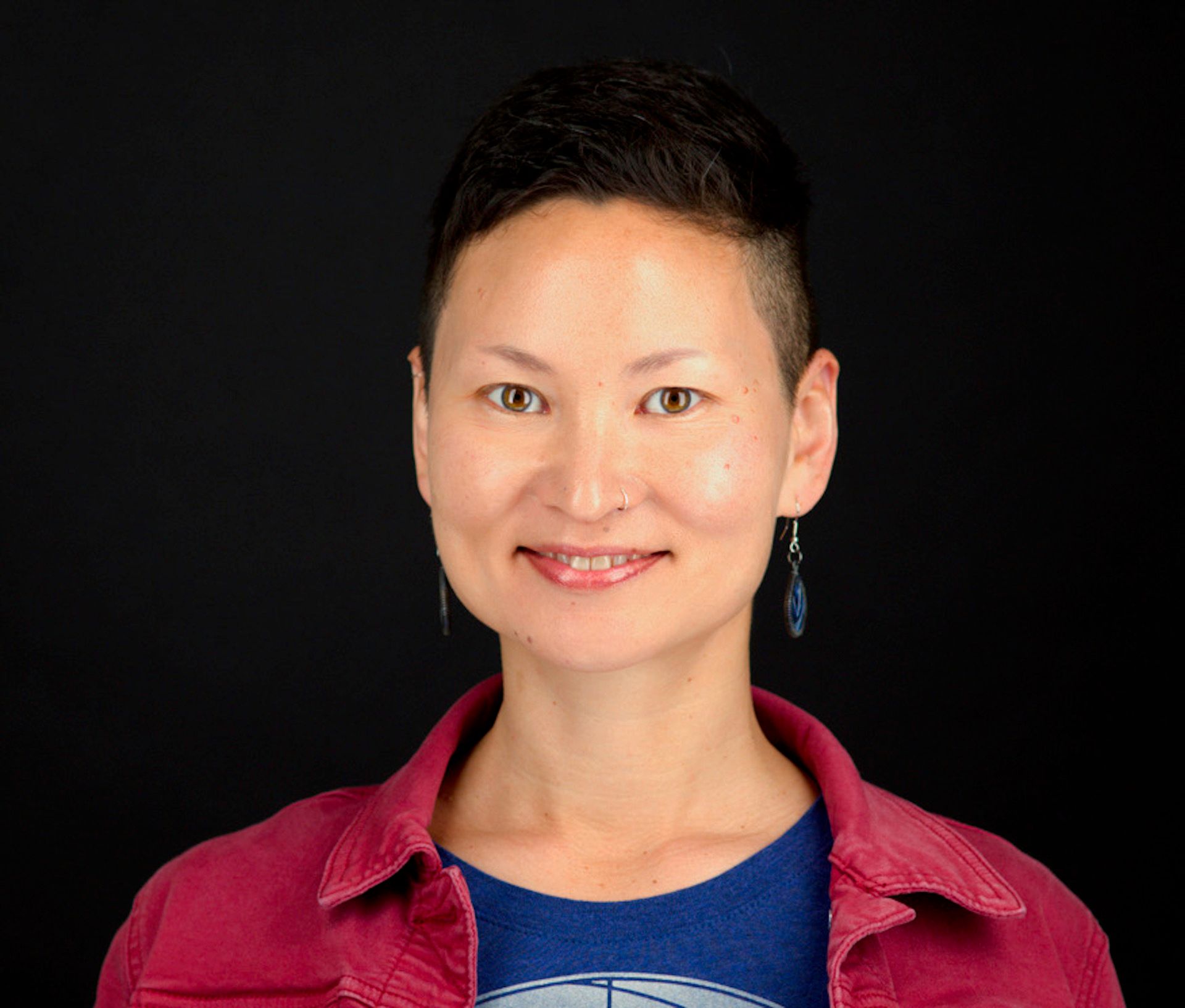 Perrine, a Chinese-American person with short hair, wearing a blue shirt and red jacket.