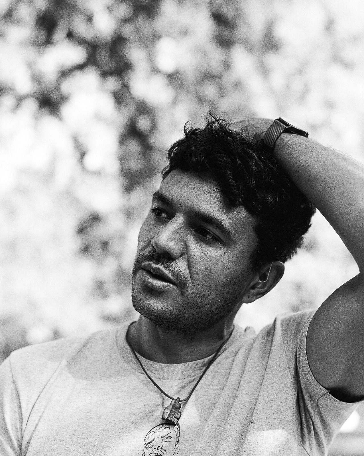 A black and white photo of the poet's head and shoulders, in a white t-shirt, one hand on his head, looking out of the frame