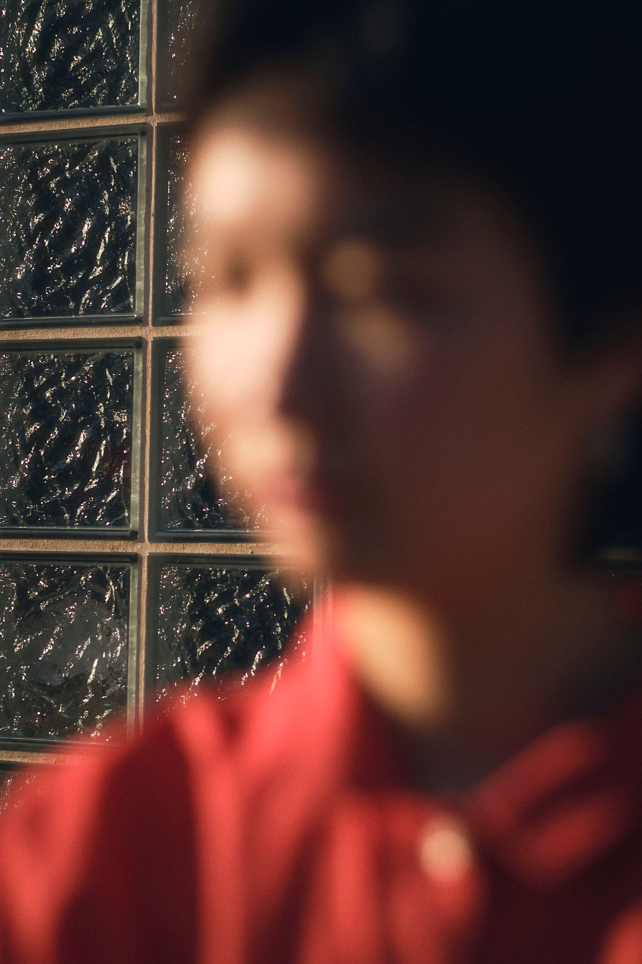 Ruby Que, an Asian person with short black hair, steps out of focus in front of a glass brick wall.